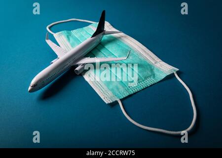 viaggio sicuro durante la pandemia del coronavirus. modello di aeroplano con maschera facciale su sfondo blu Foto Stock