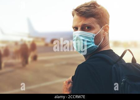 viaggio durante la pandemia del coronavirus - giovane uomo che indossa la faccia protettiva maschera e aereo d'imbarco all'aeroporto Foto Stock