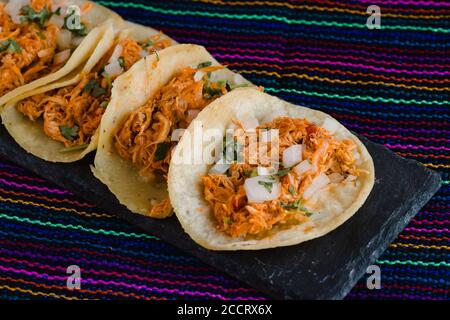 Tacos messicani pieni di tinga de pollo su un tradizionale sfondo tessile Foto Stock