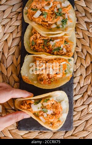 Tacos messicani in fila e una mano che ne tiene uno Foto Stock