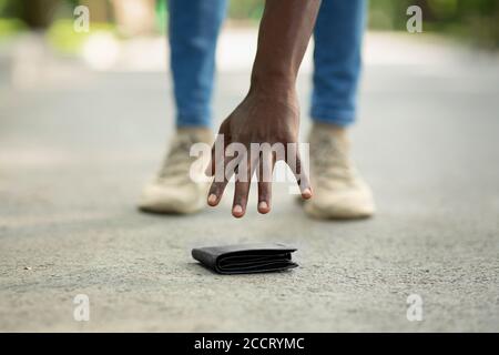 Vista ravvicinata del ragazzo nero che raccoglie il portafoglio perso sulla strada della città Foto Stock