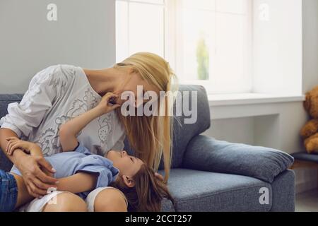 La madre felice e il figlio del bambino giocano a coccolare sul divano in camera Foto Stock
