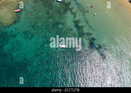 Vista aerea del drone delle acque calme e poco profonde del mare una giornata estiva di sole. Persone che nuotano nell'acqua limpida del mare, barche ancorate, riflessi del sole sulle increspate Foto Stock