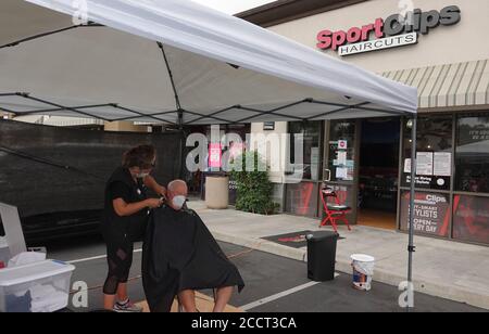 Un uomo più anziano sta ottenendo un taglio di capelli all'esterno come Sport clip parrucchiere spostato le operazioni all'aperto per evitare Covid-19 arresto. Foto Stock