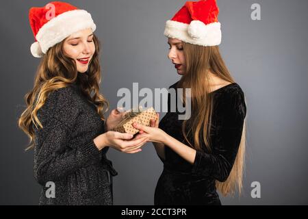 Due giovani donne scambiano regali per Natale. Due belle bionde in Babbo Natale cappelli dare un mestiere confezione regalo da mano a mano. Foto Stock