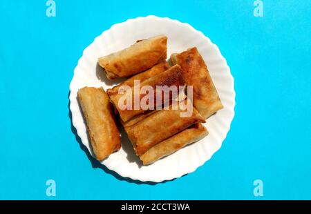 Famosa cucina tradizionale mediorientale, asiatica. Involtini di primavera di verdure su sfondo blu brillante. Molti rulli a molla su piastra bianca. Vista dall'alto Foto Stock