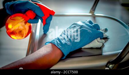 Mani di una donna nera che pulisce una sedia. Messa a fuoco selettiva sul guanto in primo piano. Sfondo sfocato. Prevenzione di Covid-19 Foto Stock