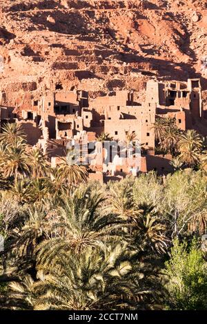 Resti di un antico villaggio marocchino con i suoi edifici parzialmente ridotti in adobe e un gruppo di palme in primo piano. Concetto di viaggio Foto Stock