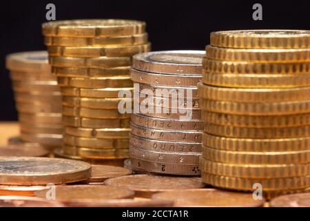 Pile di monete in euro con monete sfocate in primo piano e uno sfondo nero Foto Stock