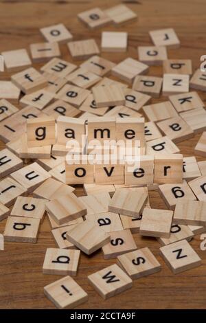 Lettere di legno che compongono le parole 'game over' su uno sfondo di lettere sparse versate su una tavola di legno Foto Stock