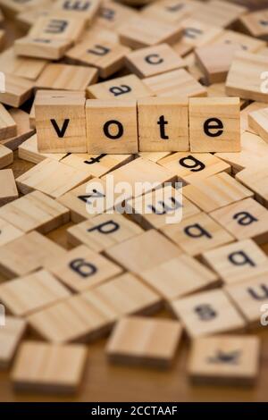 Lettere di legno che compongono la parola 'voto' su uno sfondo di lettere sparse versate su una tavola di legno Foto Stock