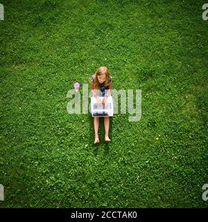 Bambina bionda che lavora su un computer portatile. Riproduzione di giochi o visione di film. Vista dall'alto. Vista dall'alto. Vista dall'alto Foto Stock