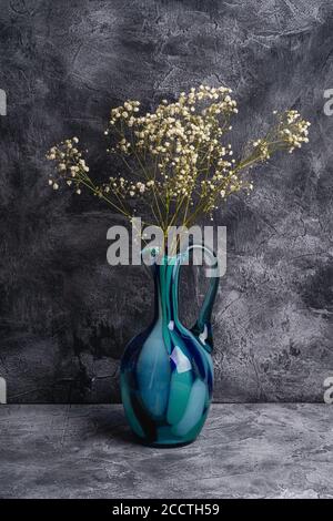 Vaso con caraffa blu con fiori bianchi secchi in gypsophila sfusi su fondo di pietra scuro a trama, vista angolare Foto Stock