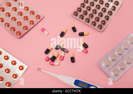 Vista dall'alto in piano di capsule di medicina, pillole e termometro su sfondo rosa, covid e concetto di influenza, spazio di copia Foto Stock