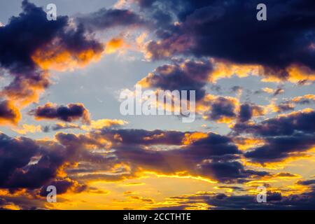 Un cielo molto drammatico pieno di gialli, blu e arance. Nuvole a contrasto durante il tramonto illuminate dal sole che tramonta. Naturale saturo luminoso Foto Stock