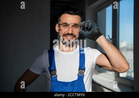 Uomo in tute e occhiali di protezione guardando la macchina fotografica e. sorridente Foto Stock