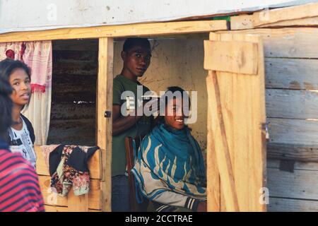 Ranohira, Madagascar - 29 aprile 2019: Sconosciuto ragazzo locale ottenere il suo taglio di capelli da un amico in negozio retro camera fatta di tavole di legno. Persone in questo p Foto Stock