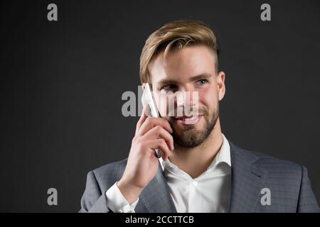 Imprenditore sorridenti utilizza lo smartphone comunicazione, sfondo nero. L'uomo parla cellulare ufficio. Uomo in tuta imprenditore assume i vantaggi delle moderne tecnologie mobili. Business il concetto di chiamata. Foto Stock