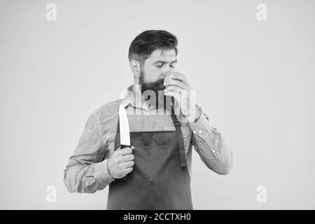 Cucina sana. Preparazione di insalate fresche. Chef professionista nel grembiule rosso. La cucina è il suo hobby. Uomo barbuto in uniforme cuoco. Casalinga sicura preparare il pomodoro. Uomo maturo tenere coltello e verdure. Foto Stock