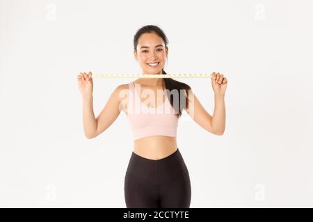 Fitness, stile di vita sano e concetto di benessere. Ritratto di sorridente ragazza asiatica bruna sport, atleta femminile in activewear mostrando metro a nastro Foto Stock