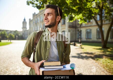 Uomo gioioso con libri di testo in piedi nel campus universitario Foto Stock