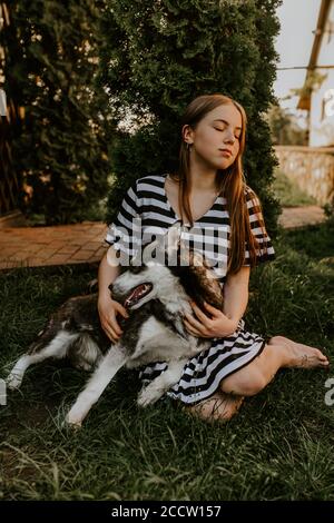 la ragazza bionda è seduta sull'erba verde con un cane husky dagli occhi azzurri