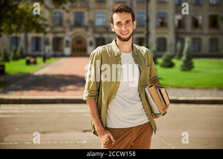 Carino gioioso moderno maschio undergraduate tenere libri Foto Stock