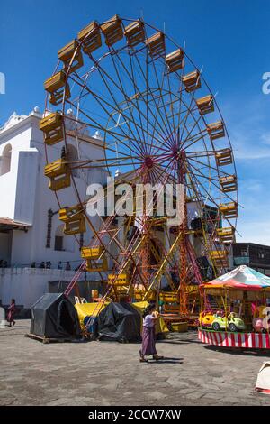 Due donne maya di Tzutujil camminano di fronte alla ruota panoramica di fronte alla Chiesa di Santiago di Santiago Atitlan, Guatemala. Il siero di ferro Foto Stock