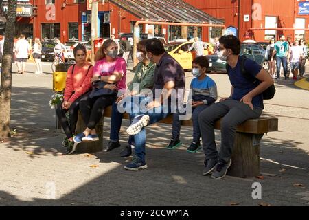 Una famiglia seduta su una panca che indossa maschere facciali protettive all'aperto durante la pandemia COVID19, Granville Island, Vancouver, BC, Canada Foto Stock