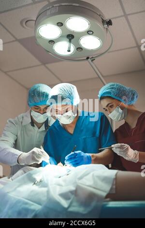 Gruppo di chirurghi al lavoro che operano in sala operatoria. Medicina di rianimazione team indossando maschere di protezione tenendo in acciaio strumenti medici Foto Stock