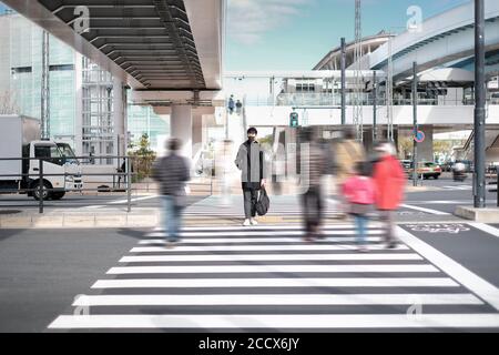 Il giovane indossa una maschera nera e aspetta di attraversare strada sotto il ponte di cemento vicino alla stazione ferroviaria elettrica Foto Stock