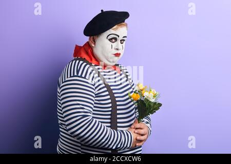 Triste depresso artista mime tenendo un bouquet di fiori isolati su sfondo blu. Depressione, solitudine, sensazione negativa ed emozione. Copia spazio Foto Stock