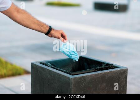 Uomo gettando la maschera chirurgica usa e getta usata di protezione nella spazzatura cassonetto Foto Stock