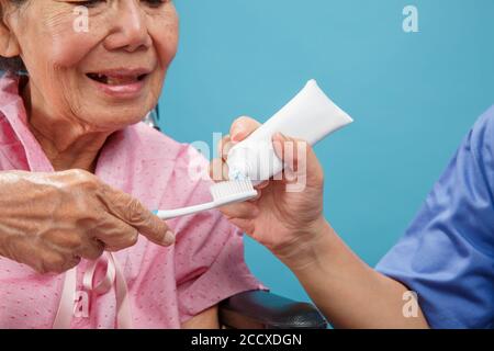 Chi si prende cura di una donna anziana asiatica mentre usa lo spazzolino da denti. Foto Stock