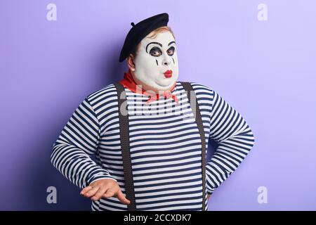 divertente clown sicuro che tiene la mano sull'anca chiedendo a calmati. isolato sfondo blu, studio girato. Foto Stock