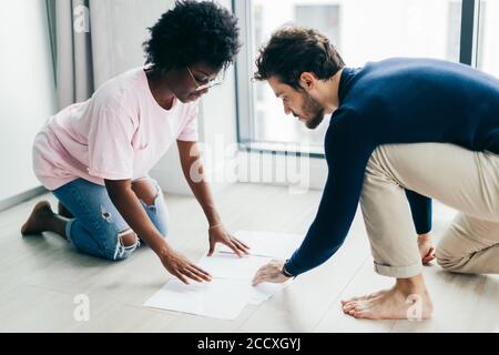 Interracial giovane coppia di sposi si siedono sul pavimento del loro affittato appartamenti, occupato con la composizione di relazione finanziaria per il servizio di assistenza fiscale, utilizzando p Foto Stock