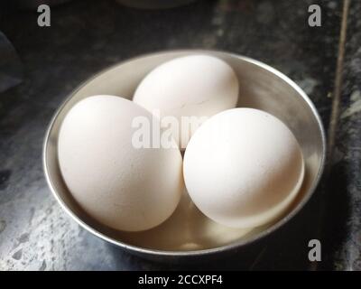 Tre uova di pollo in una ciotola su pavimento piastrellato. Messa a fuoco selettiva. Luce brillante. Foto Stock