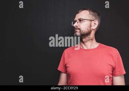 Un ritratto di profilo di un uomo maturo con capelli grigiastri e occhiali contro sfondo nero della parete Foto Stock