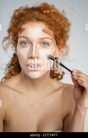 Attraente signora dai capelli rossi usando un pennello per il trucco Foto Stock