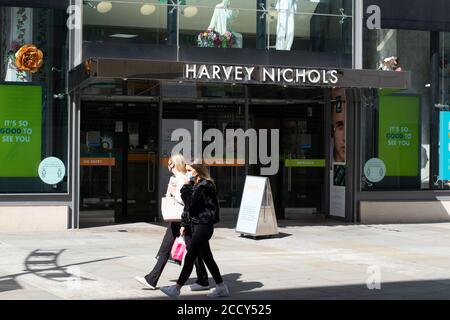 Ingresso al grande magazzino Harvey Nichols, Manchester UK, con due donne in maschere a piedi Foto Stock