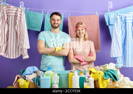 felice sorridente giovane coppia positiva con le braccia incrociate che si sentono eccitate dopo aver finito di fare la pulizia generale, primo piano ritratto isolato sfondo blu Foto Stock