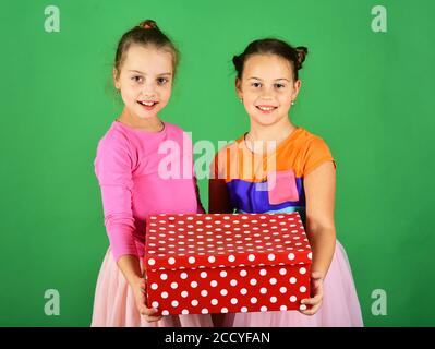 Sorelle con polka rossa punteggiata scatola regalo per la vacanza. I bambini hanno un regalo per Natale. Le ragazze con i volti sorridenti felici posano con presente su sfondo verde. Concetto di vacanze natalizie. Foto Stock
