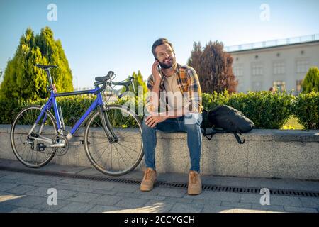 Uomo gioioso seduto a parlare su smartphone all'aperto Foto Stock