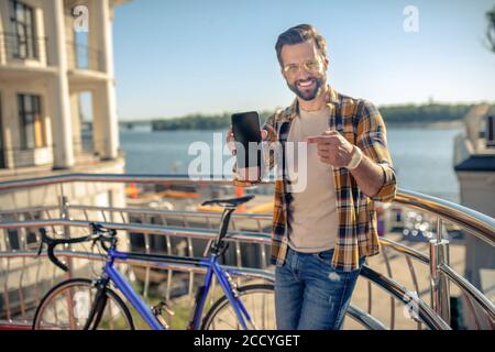 Uomo che mostra lo schermo dello smartphone mentre si è in piedi all'aperto Foto Stock