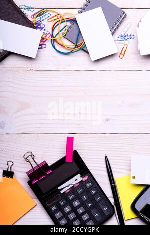 Carte vicino notebook, portafoglio, clip e penna su sfondo bianco di legno. Cancelleria e calcolatrice. Concetto di idea aziendale. Elastici colorati, perni e leganti vicino alle note adesive gialle. Foto Stock