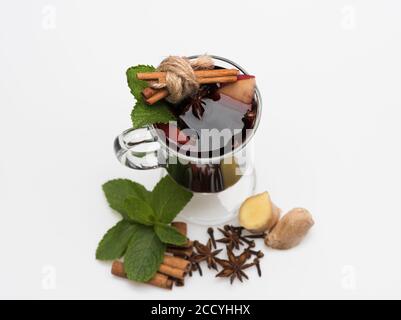 Bicchiere di vino rosso caldo su sfondo bianco. VIN brulé in vetro con decorazioni. Bastoncini di cannella, foglie di menta, anice, zenzero, fette di mela e garofano in vetro. Sommelier e degustazione di vini. Foto Stock