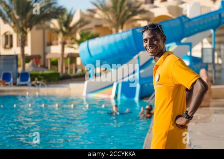 ritratto sorridente del bagnino del personale egiziano dell'hotel al nuoto area piscina sullo sfondo Foto Stock