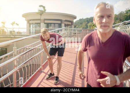 Un maschio dai capelli grigi che attraversa il ponte, un giovane maschio che tiene la mano sul petto dietro di lui Foto Stock