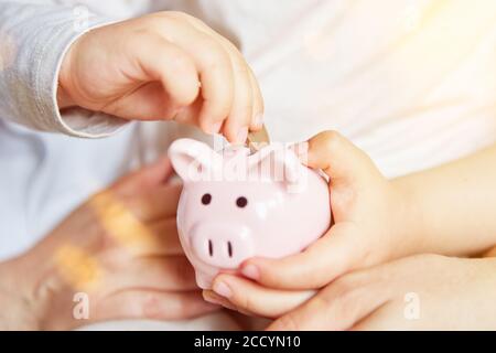 La mano del bambino mette i soldi nella banca del piggy per la fornitura in futuro Foto Stock