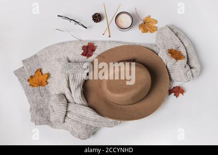 Cappello, maglione a maglia, candela e foglie gialle su tavola bianca Foto Stock